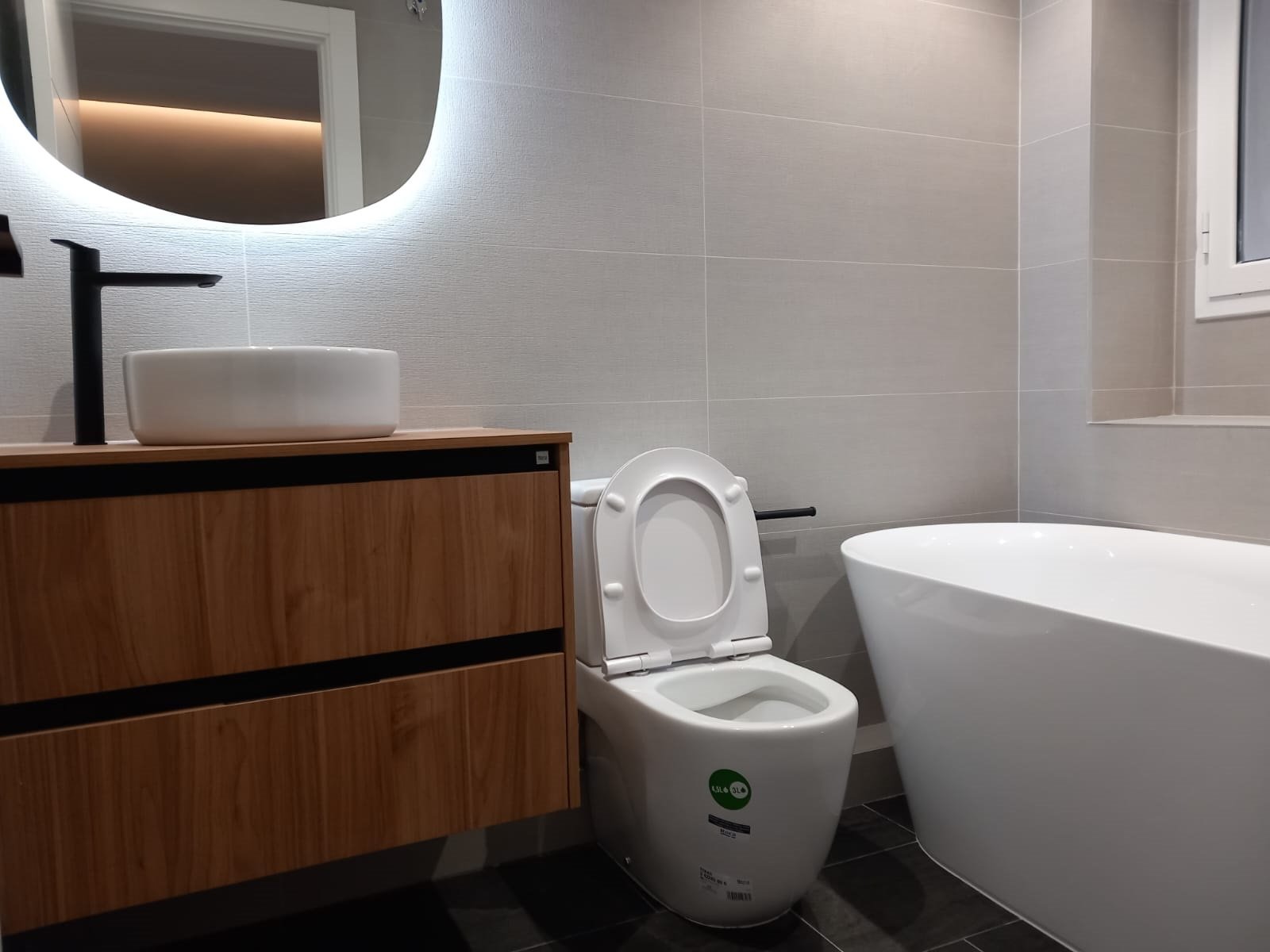 Baño con bañera exenta, espejo redondo retroiluminado y mueble de madera