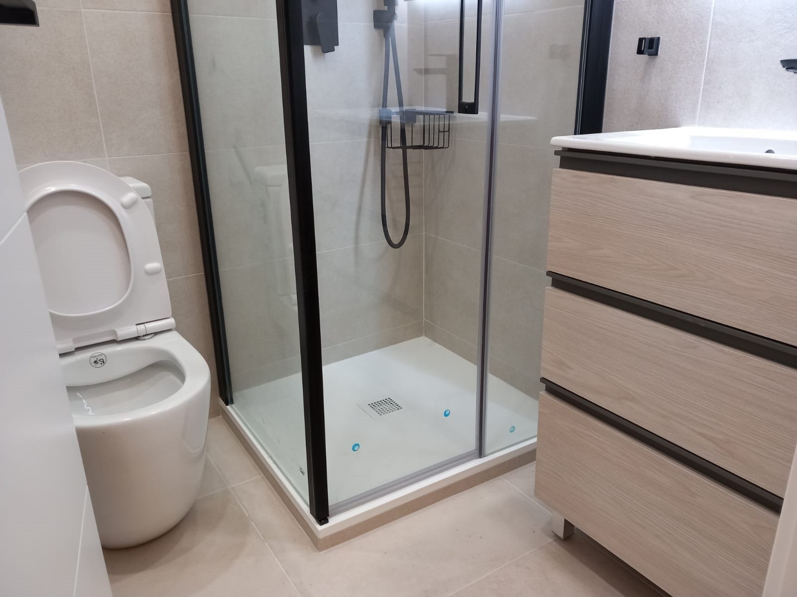Baño con ducha de obra, mampara negra y mueble de madera