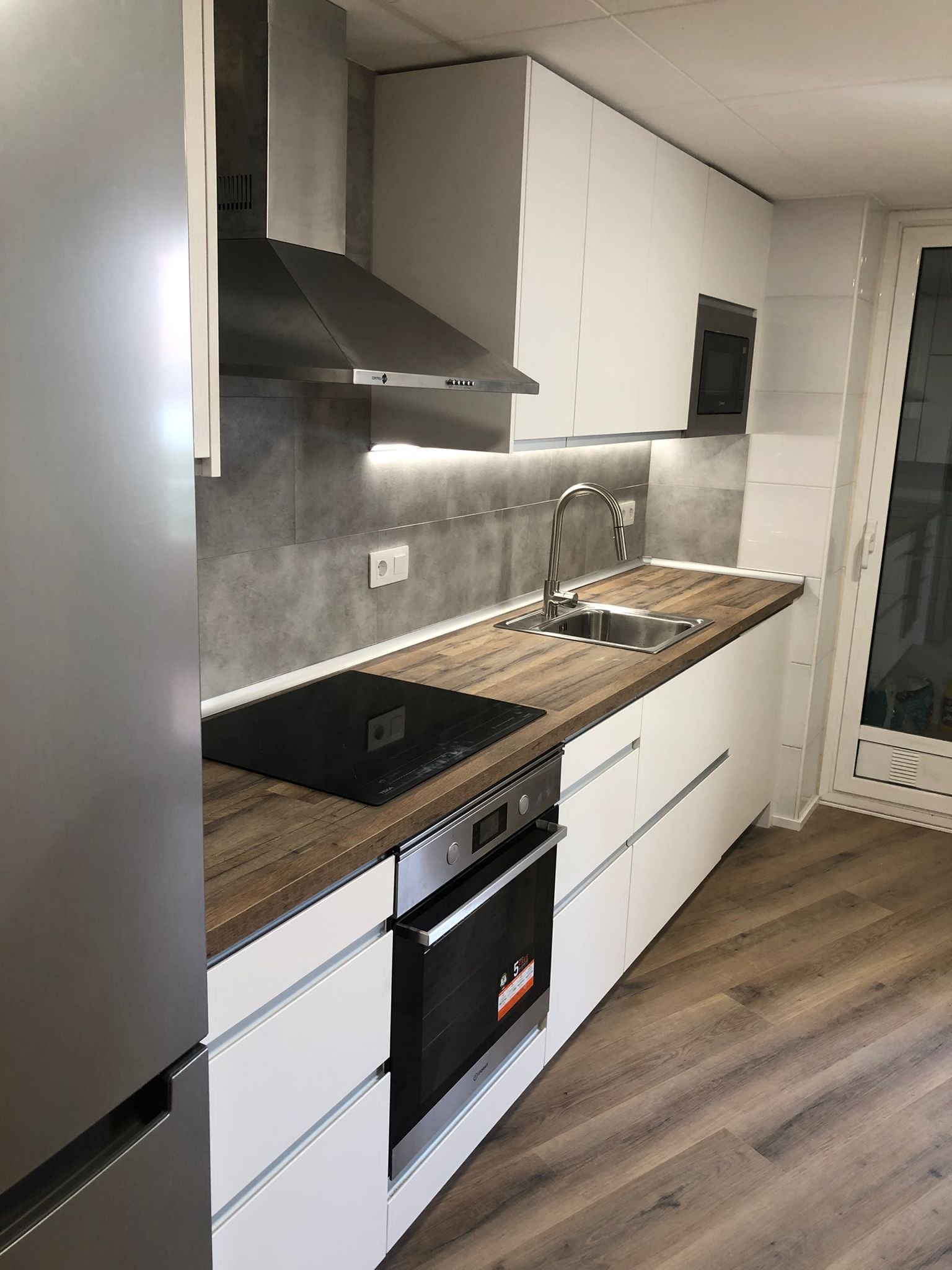 Cocina blanca con encimera de madera, campana de acero y office