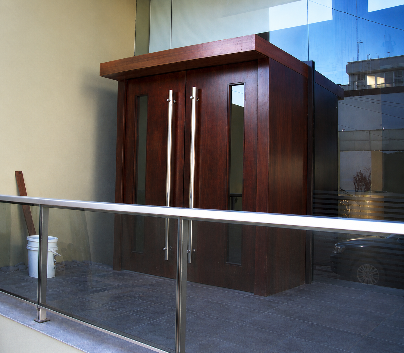 Acceso de restaurante con puerta de madera y barandilla de acero y vidrio